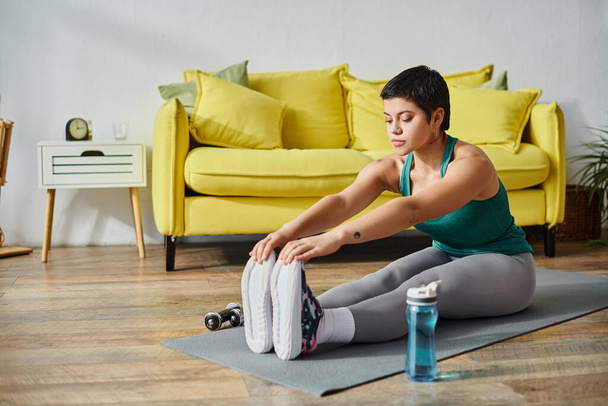 joven mujer de buen aspecto estirando sus músculos activamente en el suelo en casa, fitness y deporte - Foto, imagen