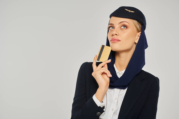 przemyślane arabskie linie lotnicze stewardessa w mundurze trzymając kartę kredytową i odwracając wzrok na szary - Zdjęcie, obraz