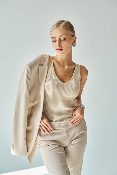 mulher jovem e sensual em roupas bege elegantes posando em fundo cinza, tiro de moda moderna - Foto, Imagem