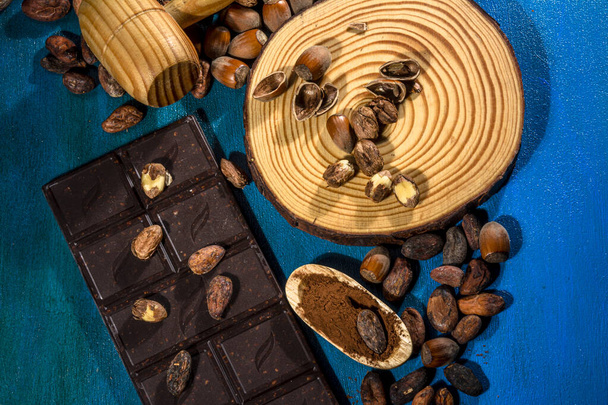 Tumma suklaa hasselpähkinät kuvattu käsin maalattu sininen tausta. Studiokuvaus. Tumma ruoka. - Valokuva, kuva