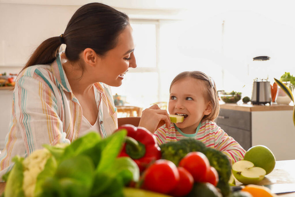 Pieni tyttö äitinsä kanssa syö omenaa keittiössä - Valokuva, kuva