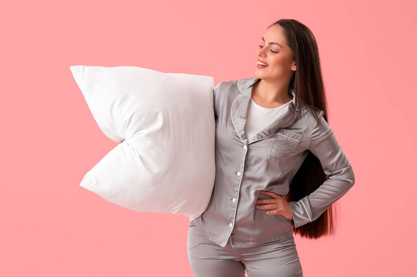 Pretty young woman in pajamas and with pillow on pink background - Photo, Image