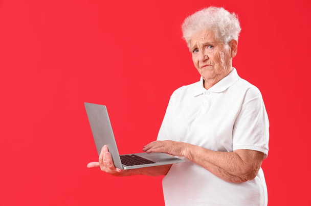 Donna anziana che utilizza il computer portatile su sfondo rosso - Foto, immagini