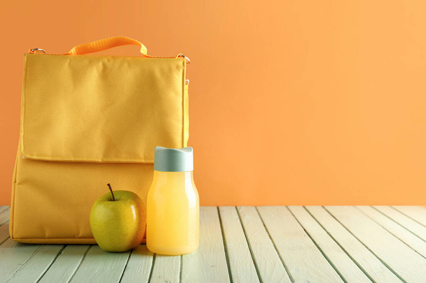 Lunchpaket mit Apfel und Flasche Saft auf grünem Holztisch neben orangefarbener Wand - Foto, Bild