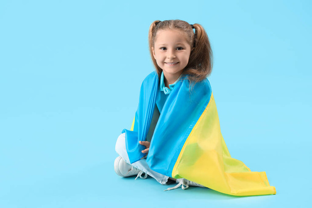 Onnellinen pieni tyttö Ukrainan lippu istuu sinisellä taustalla - Valokuva, kuva