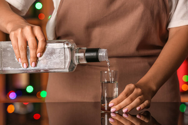 Жінка поливає холодну горілку з пляшки в постріл за столом в барі - Фото, зображення