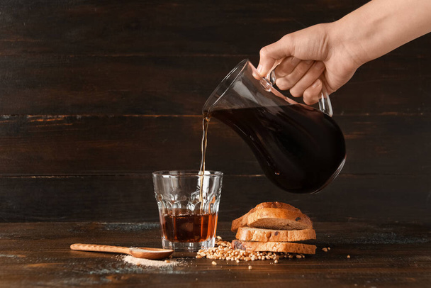 Woman pouring tasty kvass from jug into glass on wooden background - Photo, Image