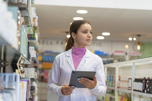 Mladá lékárnice rozhlížející se po lékárně s digitálním tabletem - Fotografie, Obrázek