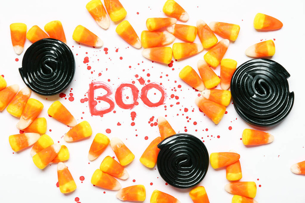 Halloween samenstelling met zoethout snoepjes, snoep maïs en woord BOO gemaakt van bloed op witte achtergrond - Foto, afbeelding
