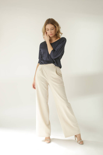 Serie of studio photos of young female model wearing simple beautiful outfit, silk satin blouse and white wide leg trousers  - Photo, Image