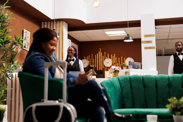 Lächelndes afroamerikanisches Hotelpersonal, das an der Rezeption steht und die Gäste mit einem Lächeln begrüßt. Freundliche Empfangsdame wartet auf Touristen, guter Kundenservice in der Gastfreundschaft - Foto, Bild