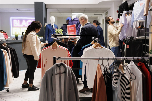 Alışveriş ve Kara Cuma günleri. Alışverişkolik çeşitlilikteki tüketiciler giyim mağazasında yeni moda kıyafetler arıyorlar, müşteriler moda mağazasını ziyaret ediyorlar, satış sezonunda alışveriş yapıyorlar. - Fotoğraf, Görsel