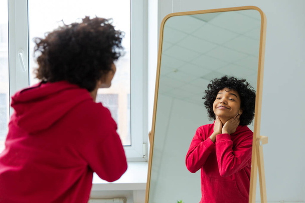 愛してる。美しい若い笑顔のアフリカ系アメリカ人女性が鏡の反射を楽しんで踊ります。黒の女性の鏡を見て自信と幸せ。自己愛の概念 - 写真・画像