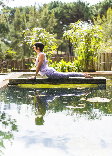 Woman practicing yoga, lying in Cobra pose (Bhujangasana exercise) outdoors. Vertical shot. - Photo, Image