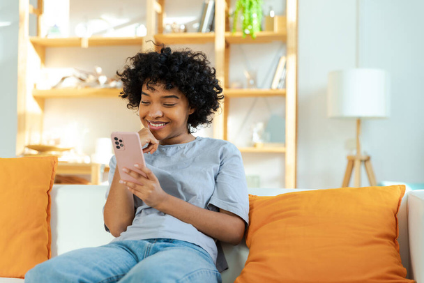 African girl holding smartphone touch screen typing scroll page at home. Woman with cell phone surfing internet using social media apps playing game. Shopping online Internet news cellphone addiction - Foto, afbeelding