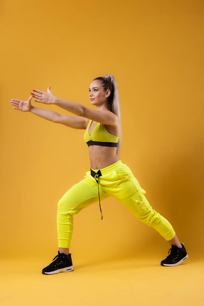 Beautiful girl in yellow outfit dancing zumba. Happy dance instructor against dark yellow or orange background. - Fotoğraf, Görsel