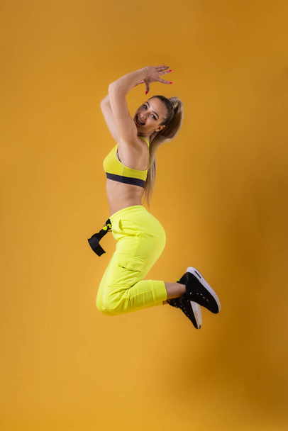 Beautiful happy girl in yellow outfit jumping against dark yellow or orange background. - Φωτογραφία, εικόνα