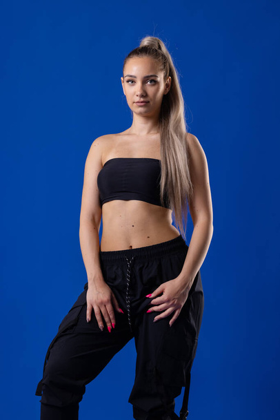 Beautiful blond girl in black outfit posing against blue background. - Zdjęcie, obraz