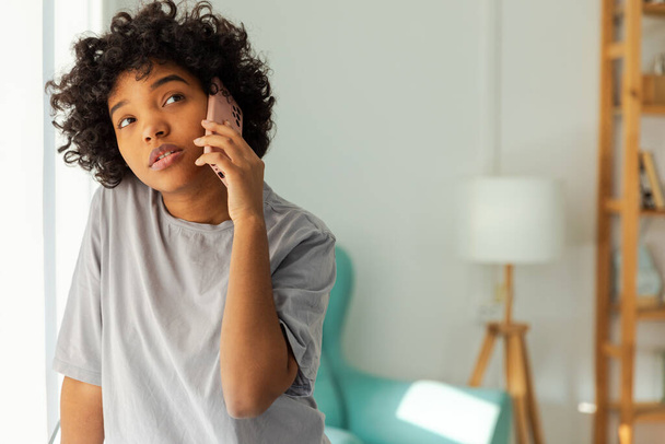 Afrikai amerikai lány beszél okostelefonon otthon. Fiatal nő, mobiltelefonnal a barátaival cseveg. Mosolygó tini lány, aki mobilon veszi fel a telefont. A hölgy mobilon beszél. - Fotó, kép