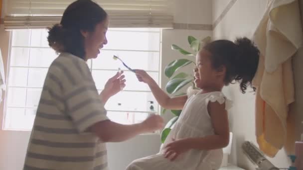 Aranyos ázsiai kislány segít anya fogmosás és játszik fogkefével, miközben szórakoztató a fürdőszobában otthon - Felvétel, videó