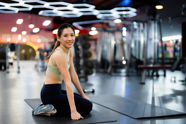 Energetikai Fitness Sportnő a Tornateremben. Ázsiai nő atléta ül és nézi a kamerát. Gyönyörű lány Cuties és bizalom Fitness Center - Fotó, kép