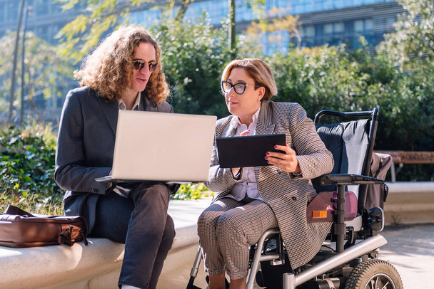 business man and woman using wheelchair working outdoors with laptop and tablet, concept of diversity and urban lifestyle - Photo, image