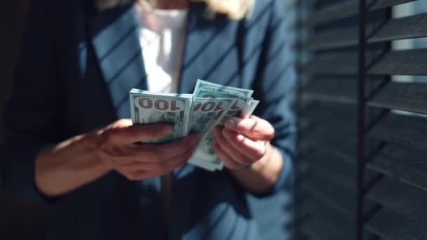 Close up of caucasian business lady dressed in formal wear counting hundreds of dollar banknotes while standing alone at office. Competent female entrepreneur planning income and expenses of company. - Footage, Video