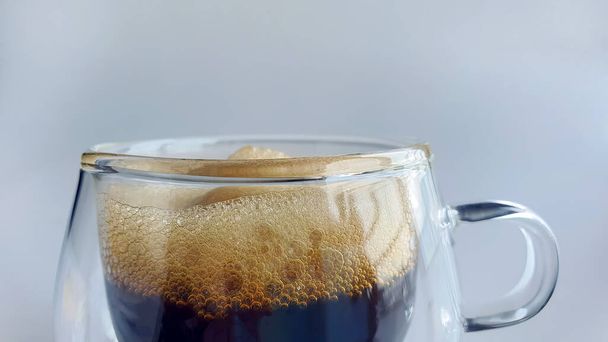 Nahaufnahme schwarzer Kaffee mit natürlichem Schaum in doppelwandigem transparentem Glas mit schlichtem Hintergrund, Morgendruck, Espresso, americano, dunkel geröstet, Robasta, Arabica, nicht Ai generiert - Foto, Bild