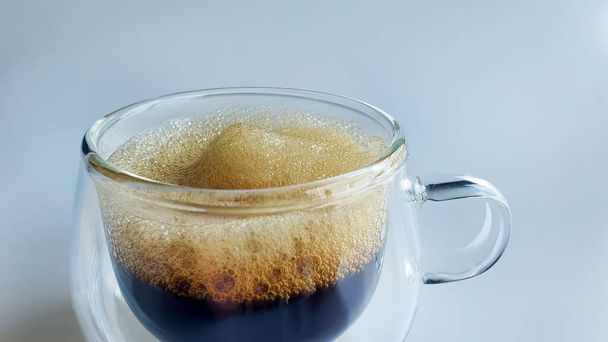 Közelkép fekete kávé természetes hab dupla falú átlátszó üveg sima háttér, reggeli boost, espresso, americano, sötét pörkölt, robasta, arabica, nem Ai generált - Fotó, kép