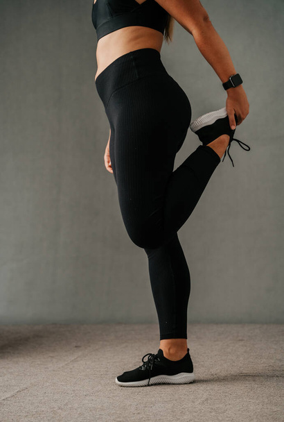 Gros plan femme échauffant ses quadriceps dans ses vêtements de sport et baskets noires. Photo de haute qualité - Photo, image