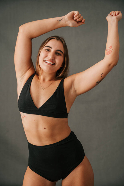 Dancing smiling Caucasian female showing off her tattoo on her arm in her active wear in the studio. High quality photo - Photo, Image