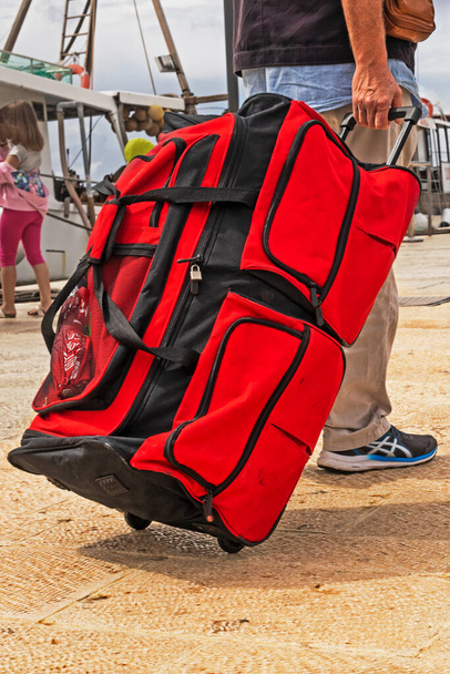 llevar una enorme maleta roja, una bolsa sobre ruedas, al muelle hasta el barco. Viajes y ocio - Foto, imagen
