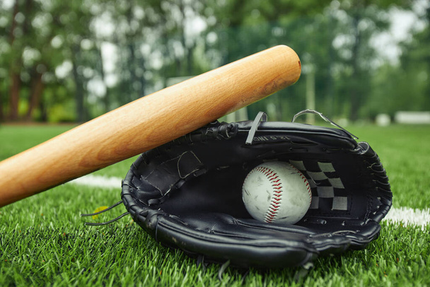 ホワイトレザー野球ボールのクローズアップビューと野球の試合のためのグリーンフィールドのバットでグローブ - 写真・画像