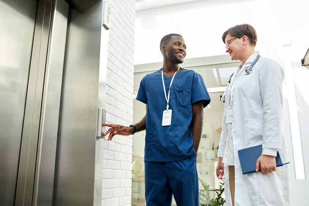 Ritratto ad angolo basso di due medici in attesa di ascensore nel moderno edificio ospedaliero e chiacchierando allegramente - Foto, immagini