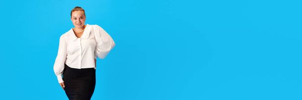 Ritratto di donna paffuta sorridente in abito elegantemente ufficiale con acconciatura stretta, capelli raccolti su sfondo blu studio. Concetto di moda, affari, carriera, professione. Bandiera - Foto, immagini
