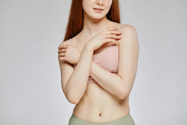Minimal abgeschnittene Aufnahme einer hellen jungen Frau, die neutrale Unterwäsche vor grauem Hintergrund trägt, bedeckt - Foto, Bild