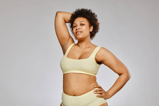 Minimale taille omhoog portret van zelfverzekerde zwarte vrouw met neutraal ondergoed tegen grijze achtergrond, body positivity concept, kopieer ruimte - Foto, afbeelding