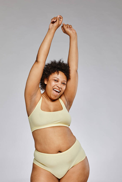 Vertical portrait of carefree black woman wearing underwear and posing happily against grey background - Fotoğraf, Görsel