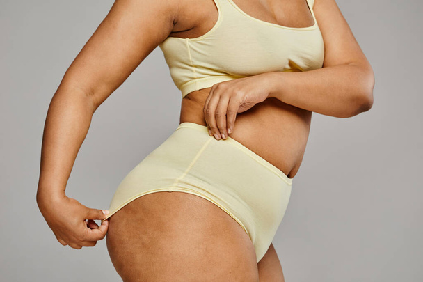Minimal cropped shot of unrecognizable black woman wearing underwear against grey background, focus on hips and cellulite, body positivity - Photo, Image