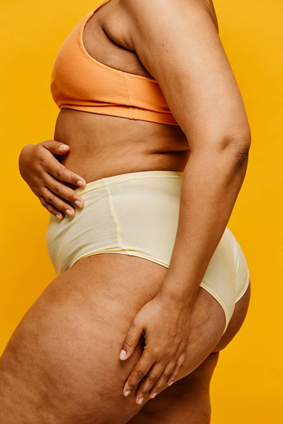 Vertikale Seitenansicht Porträt einer echten schwarzen Frau in Unterwäsche vor leuchtendem gelben Hintergrund - Foto, Bild