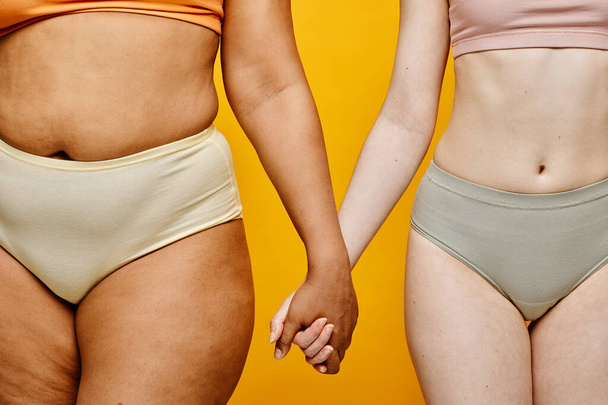 İç çamaşırı giyen ve sarı arka planda el ele tutuşan iki genç kadının farklı vücut şekillerine odaklandığı sahneler. - Fotoğraf, Görsel