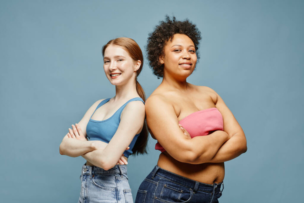 Candid cintura hacia arriba retrato de dos mujeres jóvenes seguras de pie sobre fondo azul pastel y sonriendo - Foto, imagen