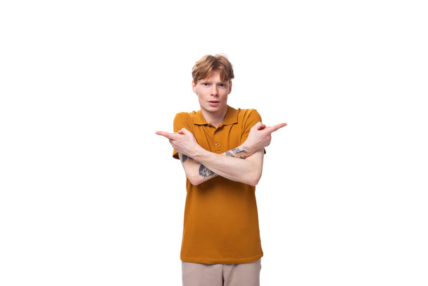 een jonge knappe roodharige man met een kapsel en een tatoeage op zijn arm is gekleed in een zomergeel t-shirt. - Foto, afbeelding