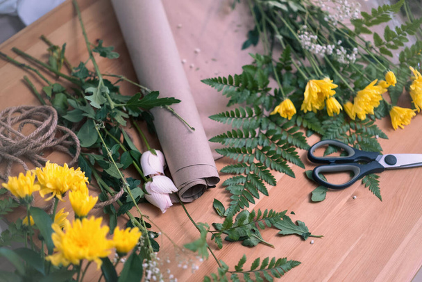 木のテーブルに黄色い花とクラフト紙の花束. フラワーショップ,春の花. - 写真・画像