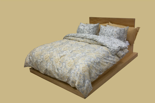 Sarı arka planda birçok yastığı, battaniyesi ve çarşafı olan ahşap çift kişilik yatak.  - Fotoğraf, Görsel