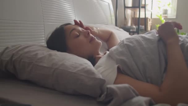 Giovane donna svegliarsi a letto, prendere smartphone e scorrere i social media al mattino a casa - Filmati, video