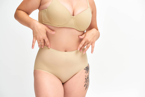 cropped view of young plus size woman in beige lingerie with tattooed hip on white backdrop - Photo, Image