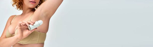 cropped view of curvy woman in lingerie applying roll-on deodorant on armpit, horizontal banner - Photo, Image