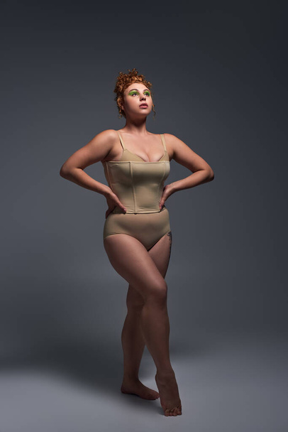 full length of young plus size model with curvy body in beige underwear on dark grey backdrop - Photo, Image