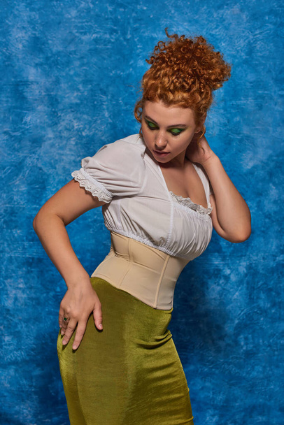 fiatal vörös hajú plusz méret modell divatos öltözék pózol kézzel csípő kék egyenetlen háttér - Fotó, kép